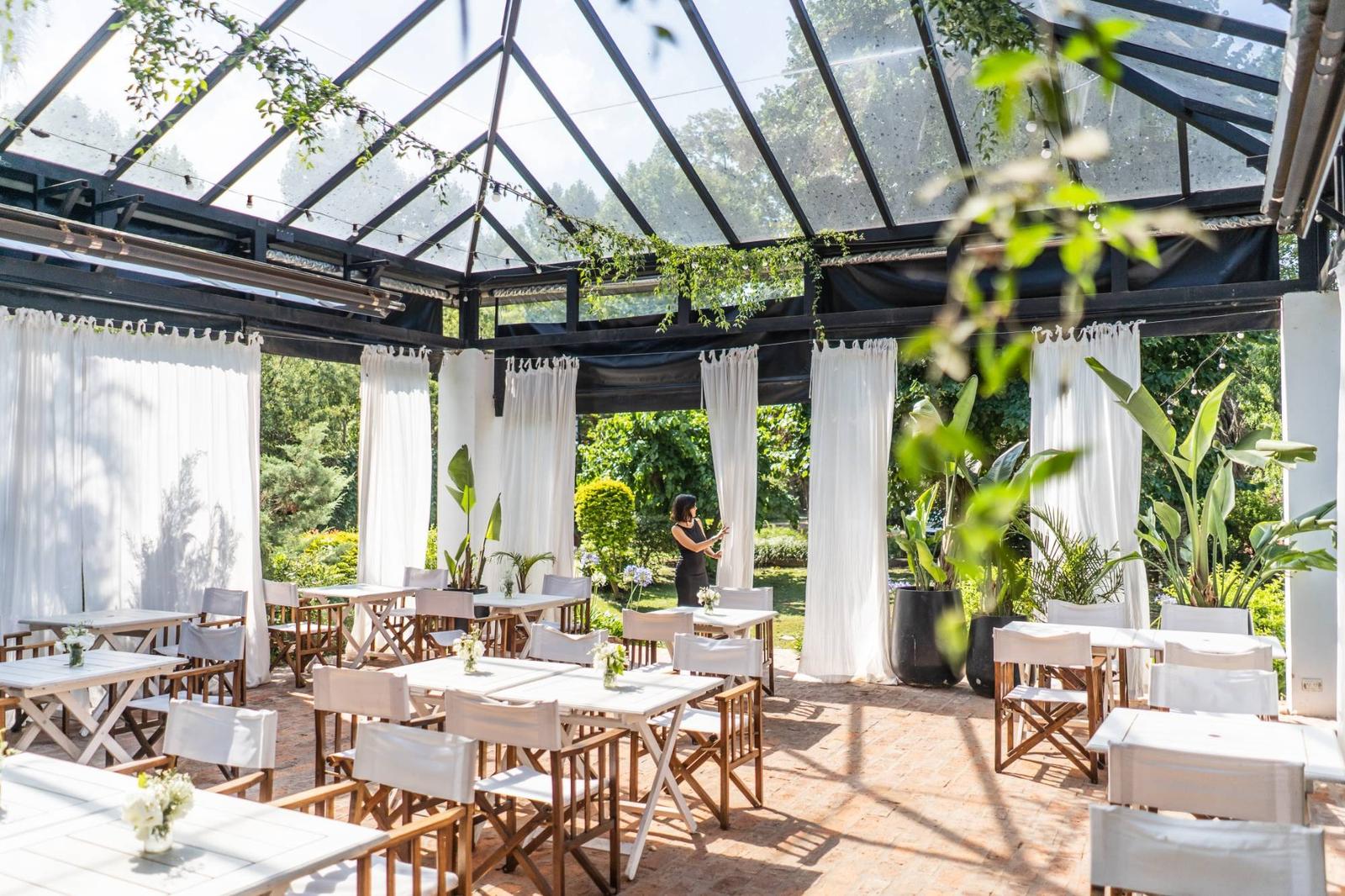 Pérgola vidriada de día, con cortinas blancas abiertas al jardín