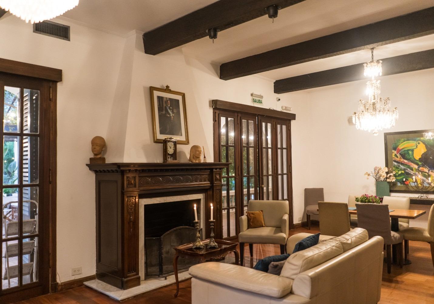 Gran salón de la casona con chimenea de madera tallada, vigas y araña de cristal