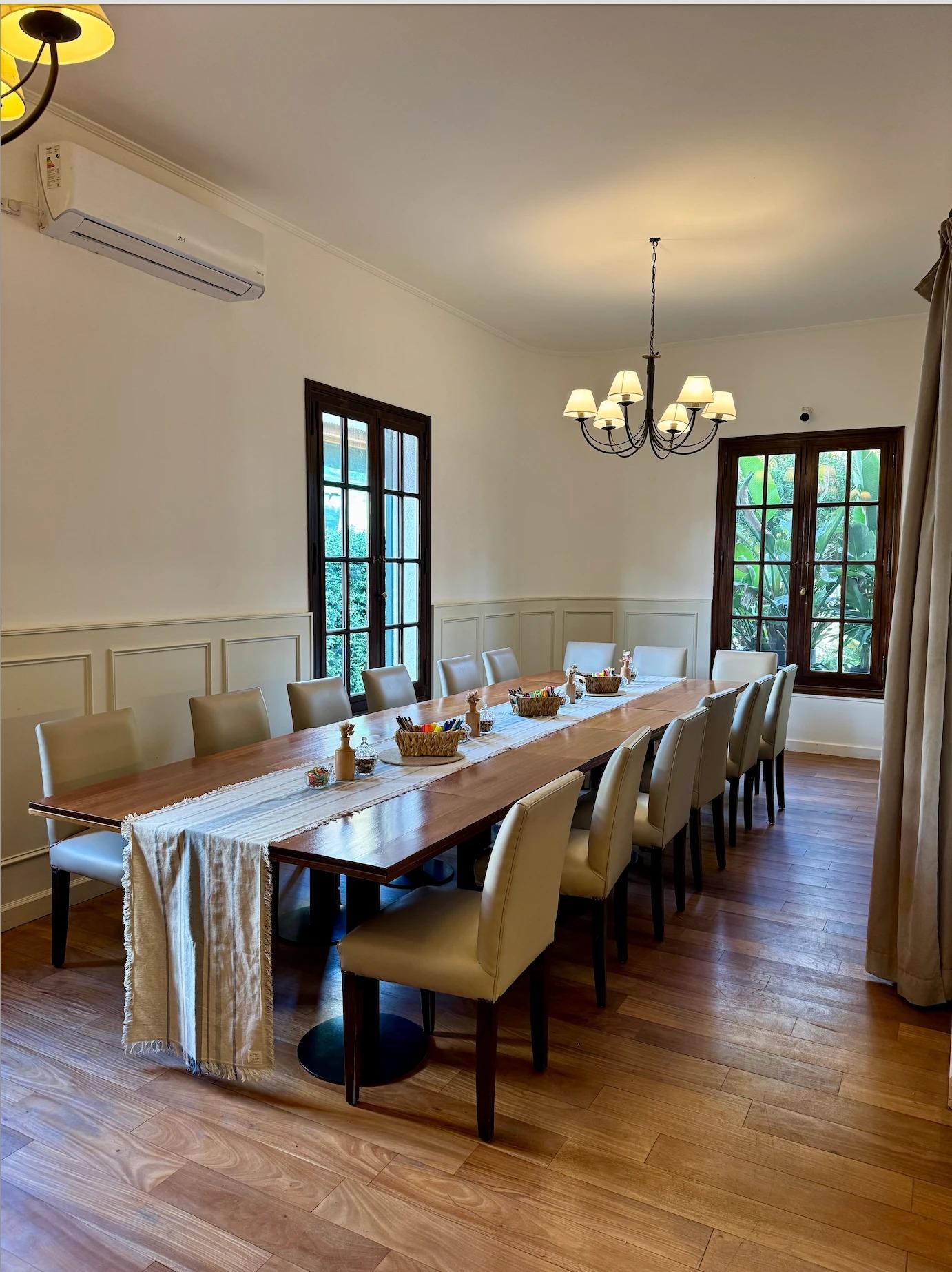 Comedor con mesa larga, araña y ventanales al jardín